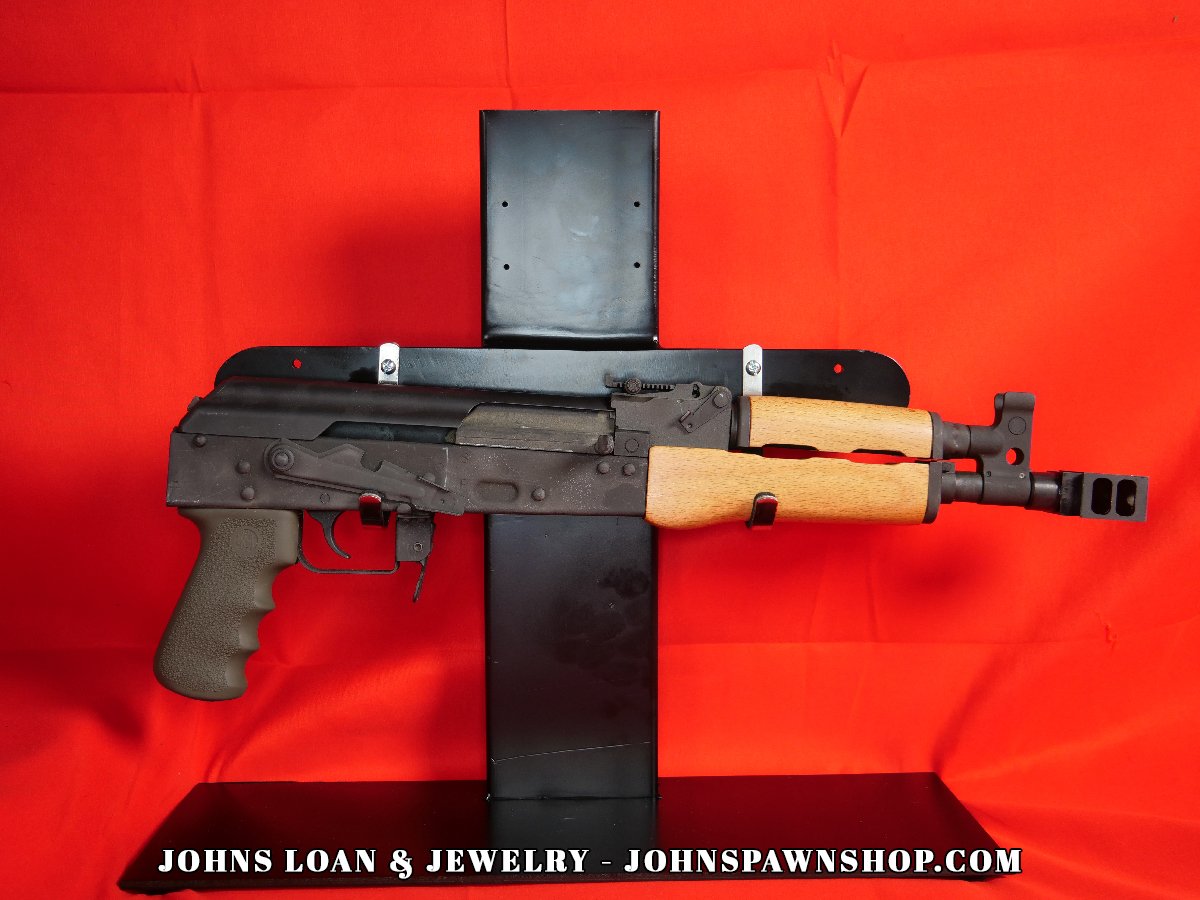 Century Arms VSKA Draco AK-47 pistol, 7.62x39mm, presented by John's Loan & Jewelry, showcases semi-automatic firearm on a display table, featuring a textured olive grip and light wood handguard.