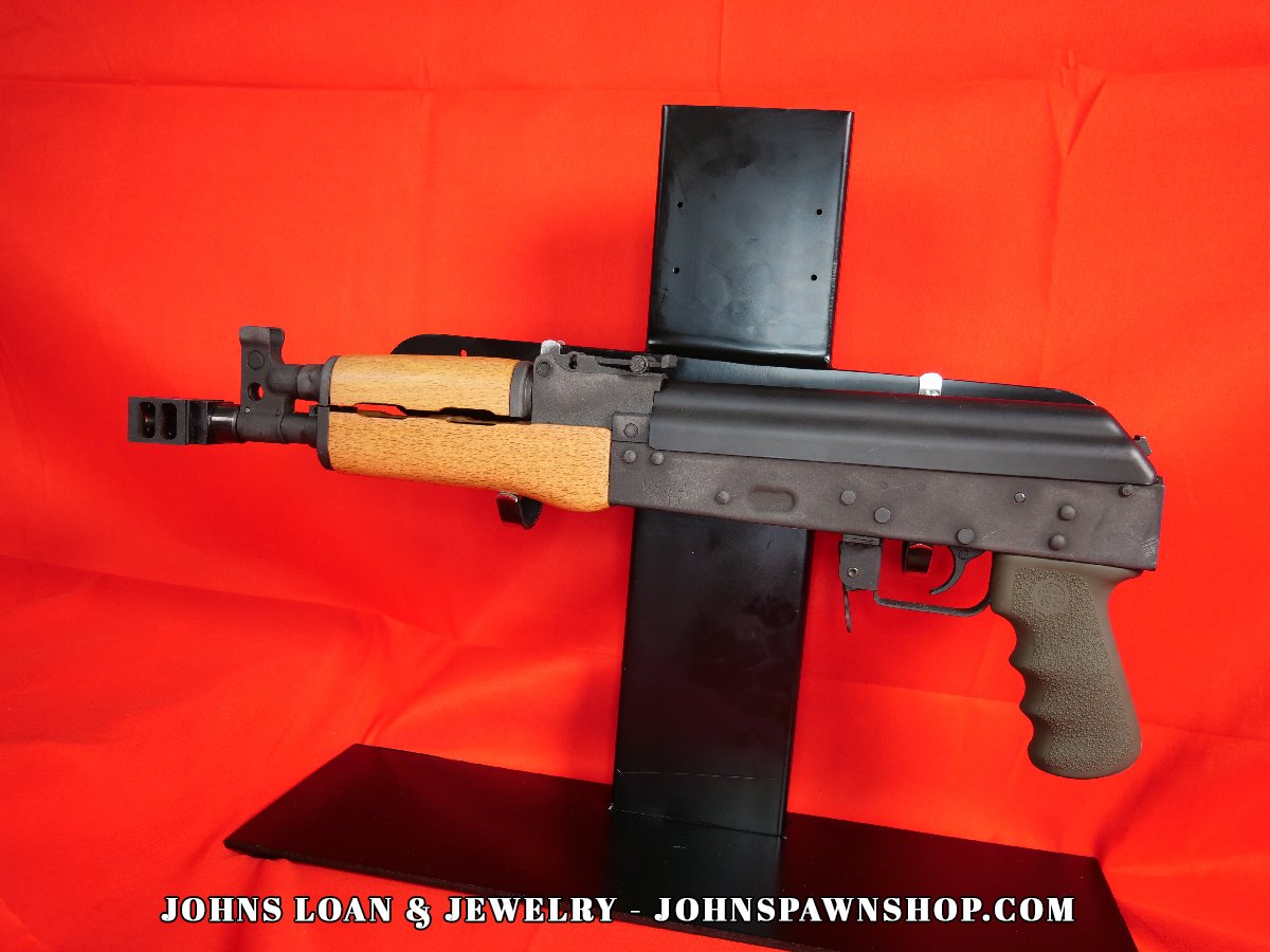 The Century Arms VSKA Draco semi-automatic AK pistol, a firearm from John's Loan & Jewelry, displayed on a table, features a distinct short barrel, textured grip, and AK magazine compatibility.