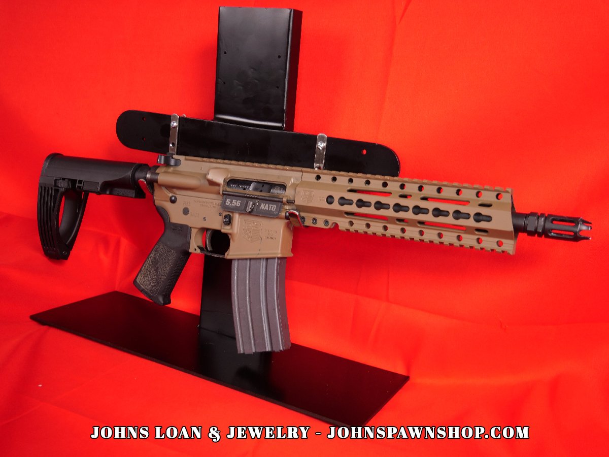 Diamondback DB15 braced AR15 pistol in FDE, chambered in .223/5.56, displayed on a table. This firearm, available from John's Loan & Jewelry, features a braced design and a 30+1 magazine.