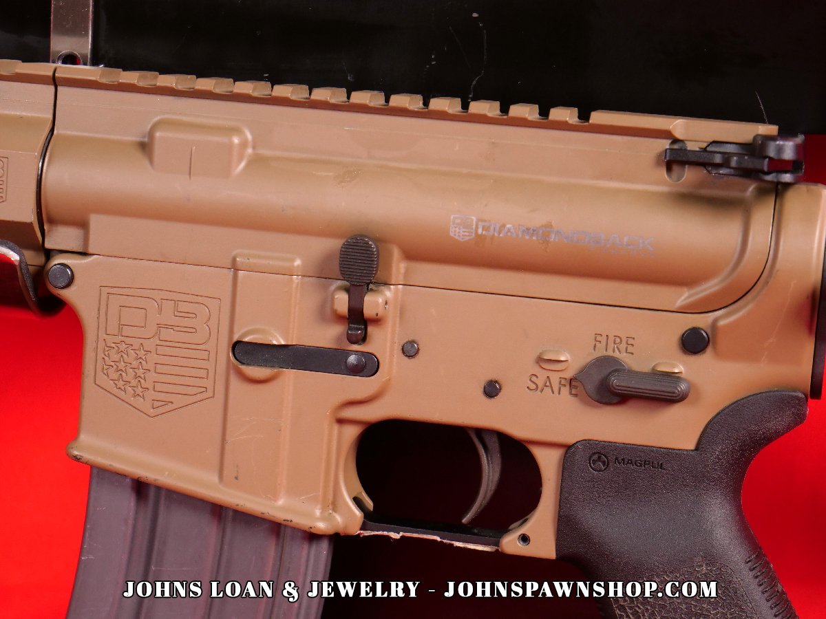 Close-up image showing the receiver of the Diamondback DB15 AR15 pistol, showcasing the firearm's FDE finish and controls. The pistol, available at John's Loan & Jewelry, features the Diamondback logo.