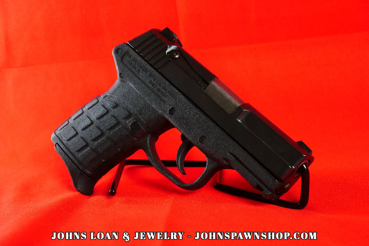 Close-up of a black KelTec PF-9 semi-auto pistol from John's Loan & Jewelry, featuring a polymer frame designed for concealment, displayed on a table against a red backdrop.