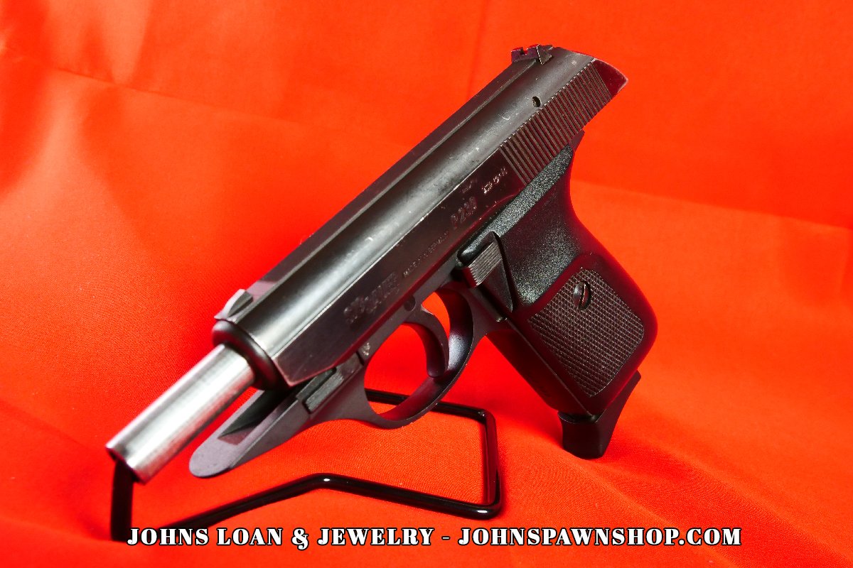 Angled view of the Sig Sauer P230, a .380 ACP pistol with a steel slide and black frame, presented by John's Loan & Jewelry, highlighting its compact CCW-nightstand design.
