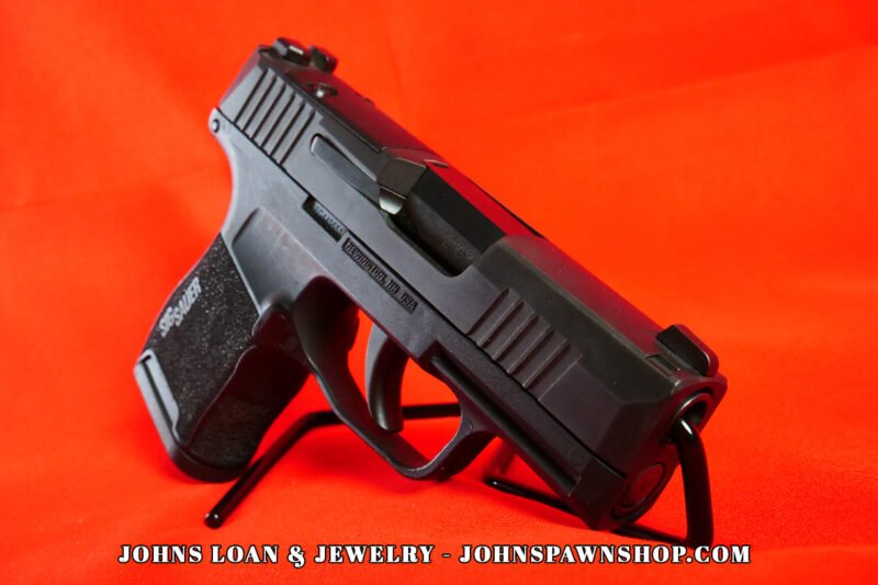 Matte black Sig Sauer P365 semi-auto pistol, angled view, showing textured grip, slide details, and XRAY3 night sights, displayed by John's Loan & Jewelry.