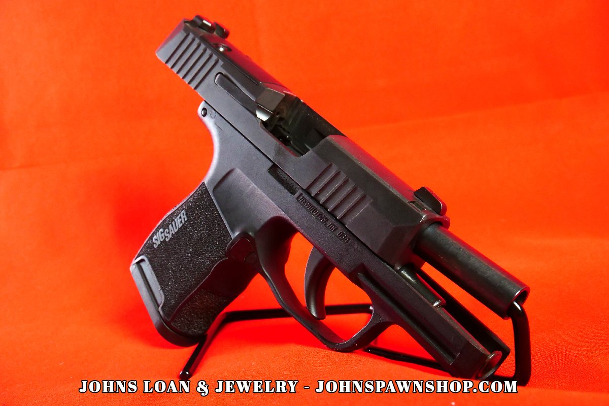Angled perspective of a matte black Sig Sauer P365 pistol, showcasing the barrel, trigger guard, and grip texture, available at John's Loan & Jewelry.