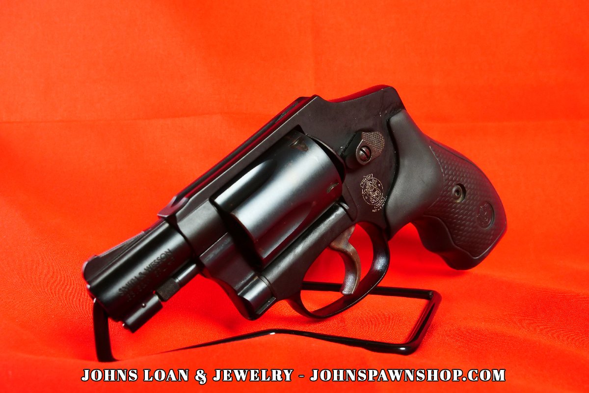Smith & Wesson 442-1 J Frame .38 Special revolver from John's Loan & Jewelry, showcasing a blued finish, textured black grip, and the iconic Smith & Wesson firearm emblem on a bright red background.