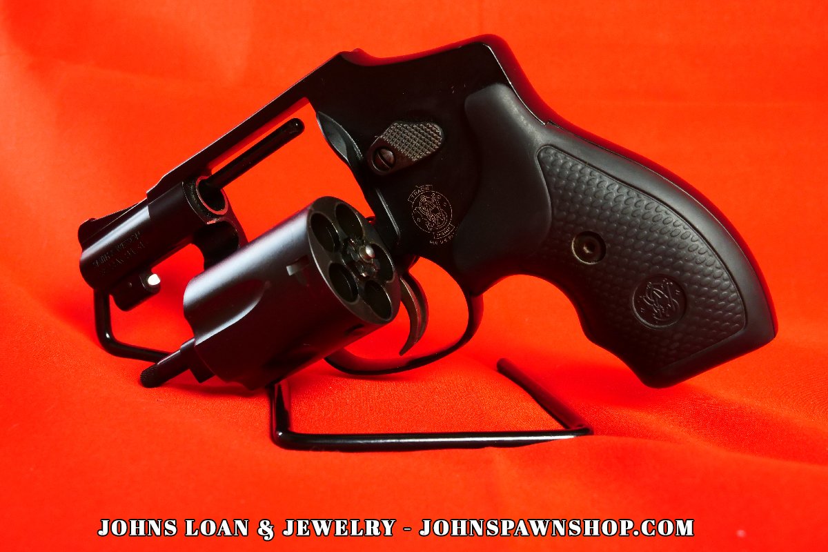 Smith & Wesson 442-1 J Frame .38 Special revolver at John's Loan & Jewelry, cylinder open, showcasing the five-shot capacity and textured black grip against a vivid red backdrop.