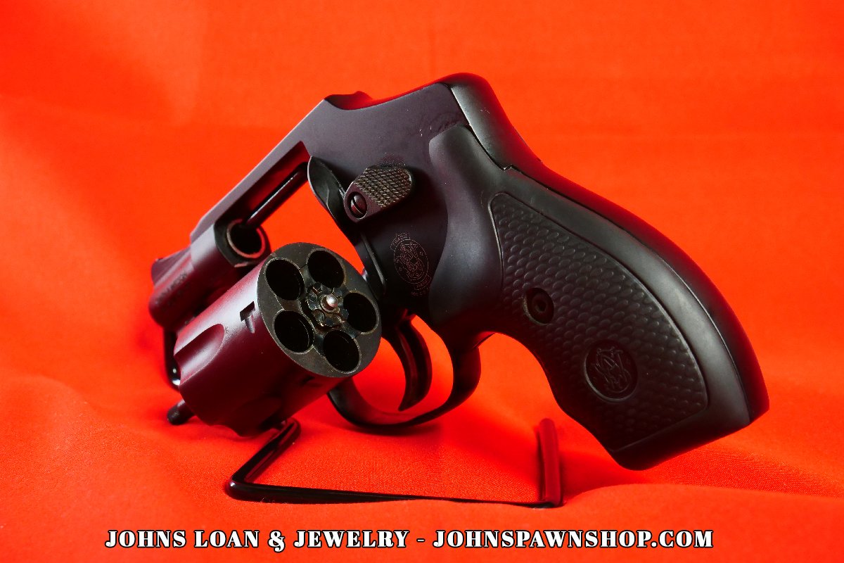 Smith & Wesson 442-1 J Frame .38 Special revolver from John's Loan & Jewelry, cylinder swung out, offering a clear view of the five-shot capacity and ergonomic grip design on a vibrant red surface.