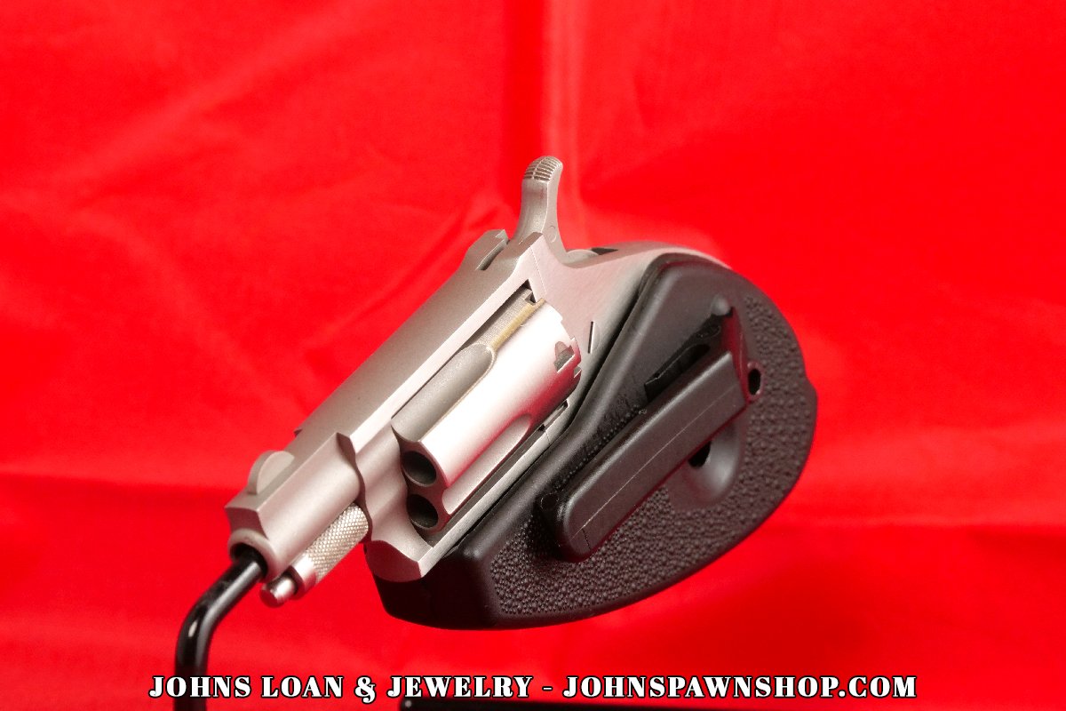 Angled view of the North American Arms .22 Magnum mini-revolver, available from John's Loan & Jewelry, displaying its stainless steel cylinder, compact frame, and integrated black holster grip.