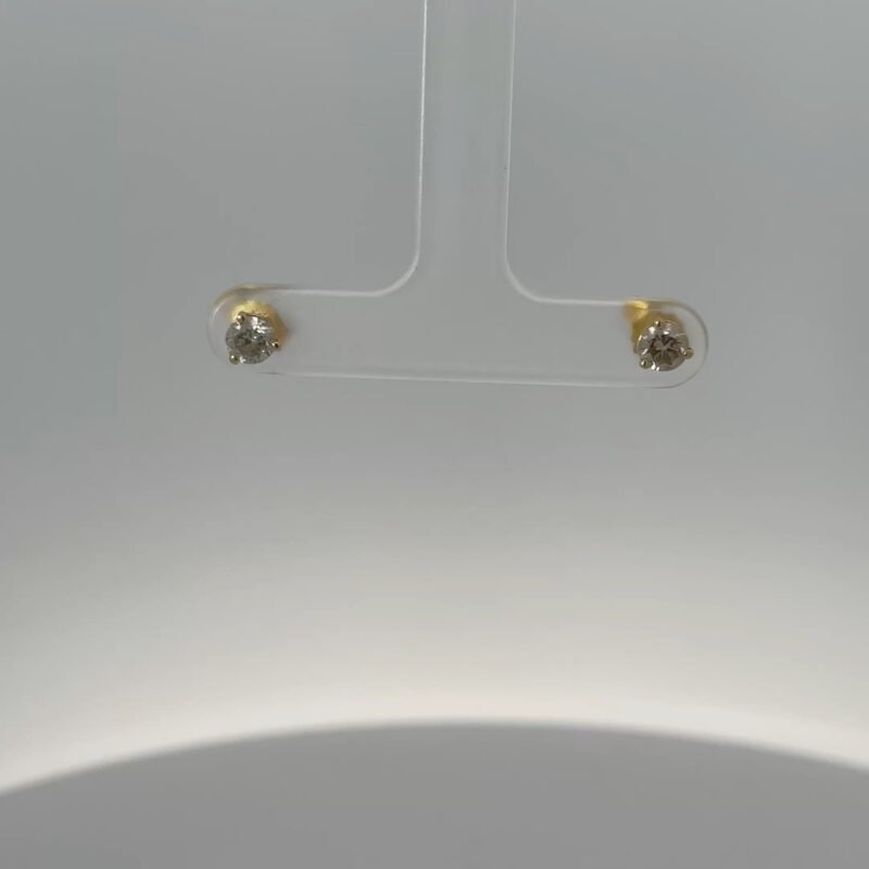 Close-up view of John's Loan & Jewelry 14kt yellow gold stud earrings, each featuring a .25ct diamond, showcased on a clear display, highlighting the jewelry's sparkle.